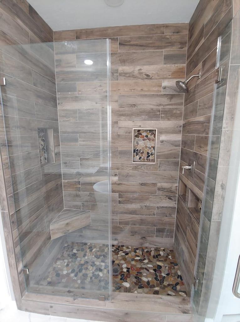 A bathroom with a walk in shower with a glass door and wooden walls.