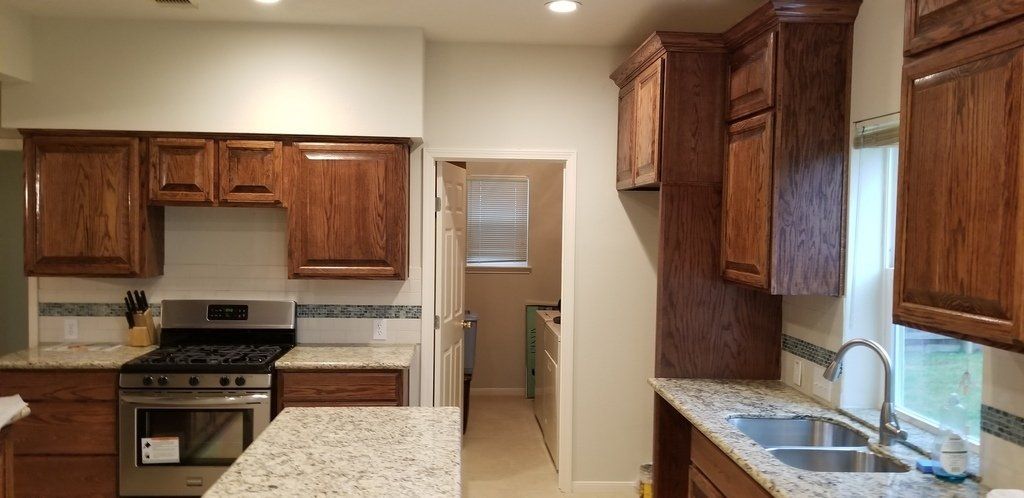 A kitchen with wooden cabinets , granite counter tops , a stove and a sink.