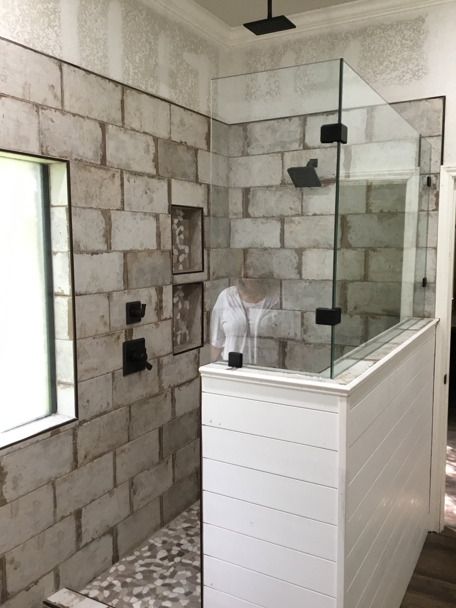 A bathroom with a walk in shower with a glass door and brick walls.