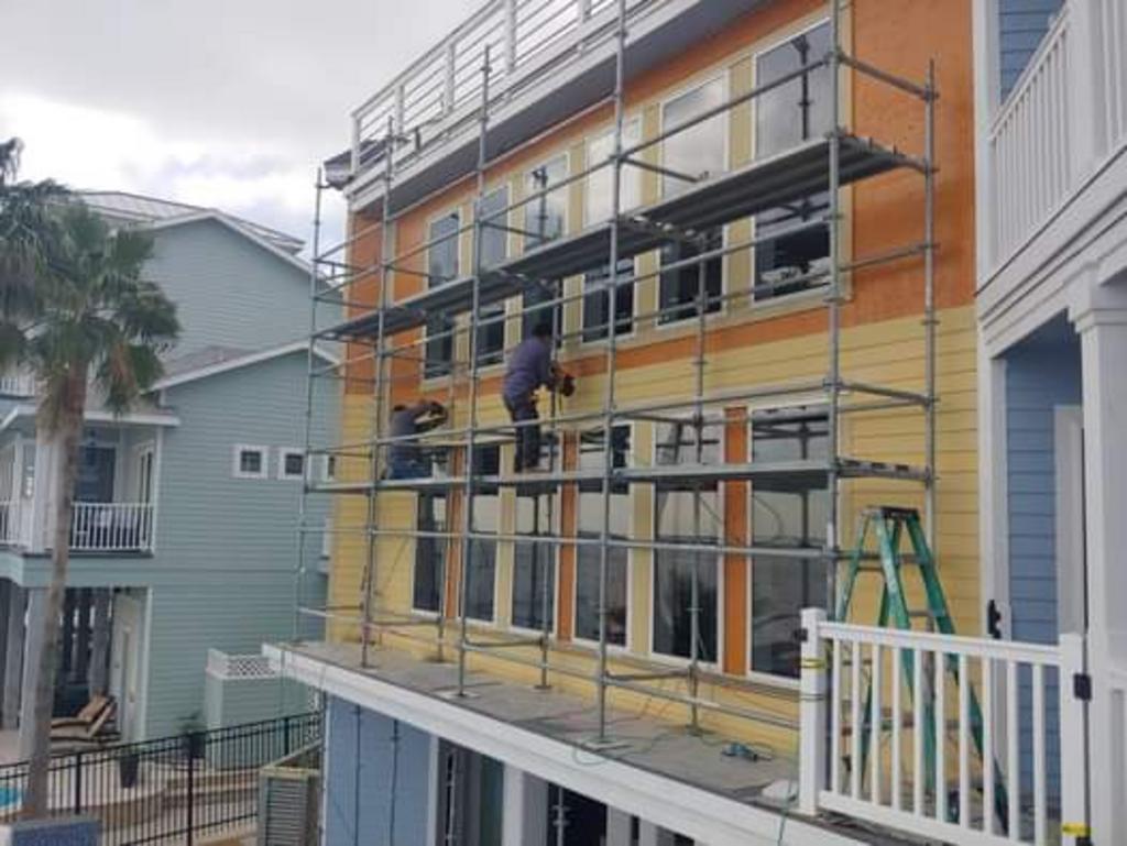 A man is painting the side of a building with scaffolding.