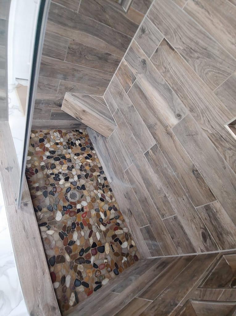 A walk in shower with wooden tiles and rocks on the floor.