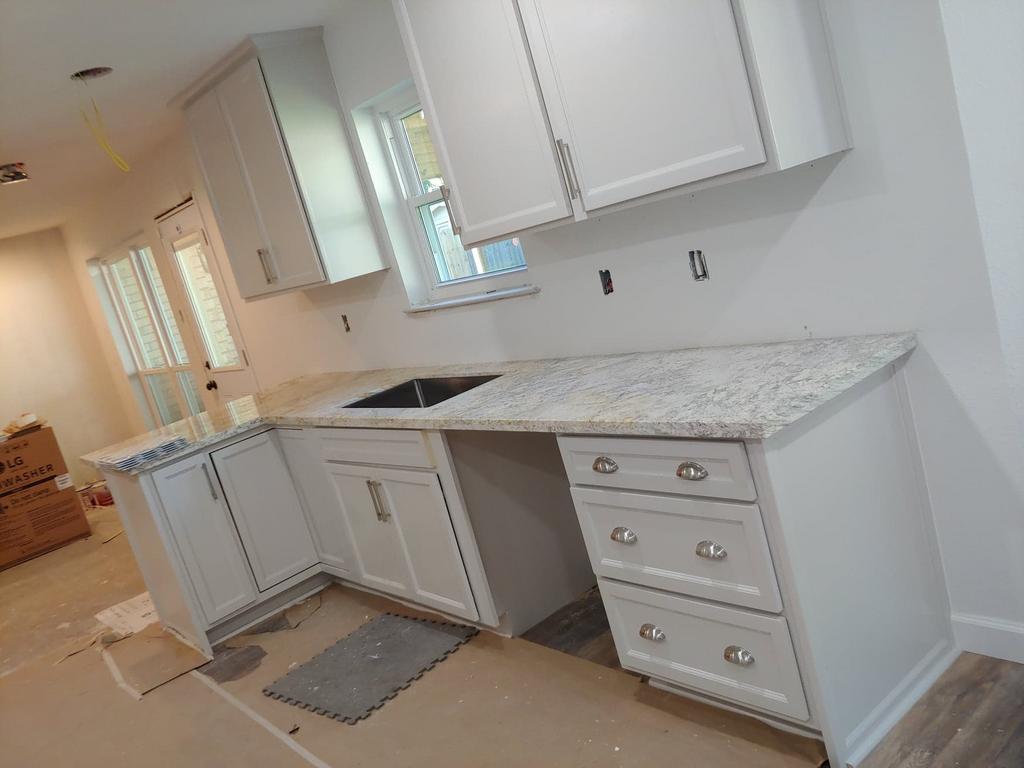 A kitchen with white cabinets , granite counter tops , and a sink.