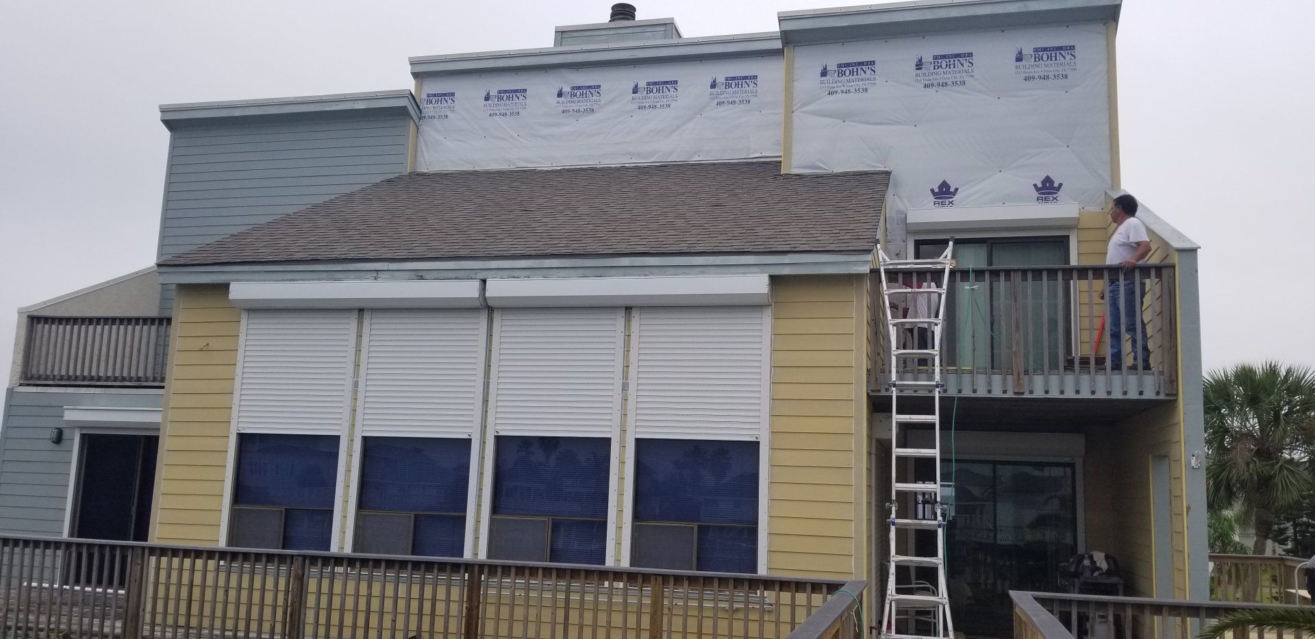 A man is standing on a balcony of a house with a ladder.