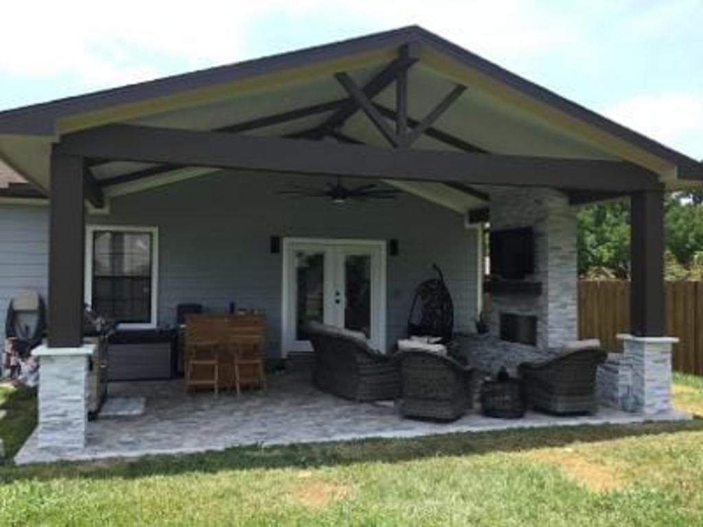 A covered patio with a fireplace and a couch and chairs under a roof.