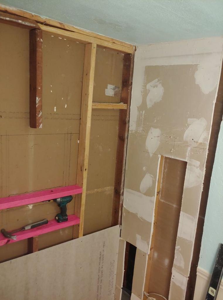 A drill is sitting on a shelf in a room under construction.