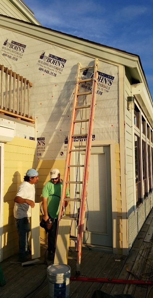 Two men are standing next to a ladder on the side of a building.