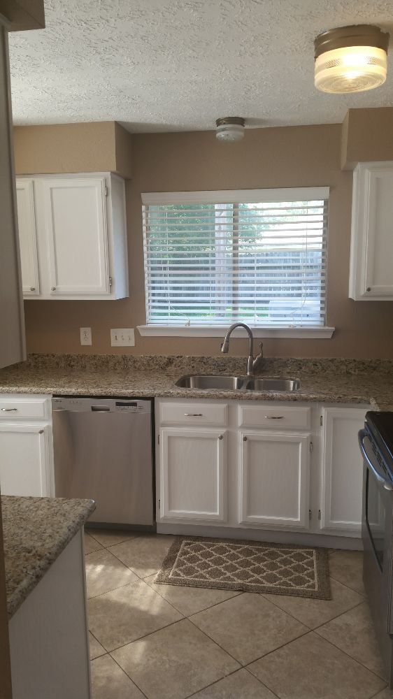 A kitchen with white cabinets , a sink , a dishwasher , and a window.