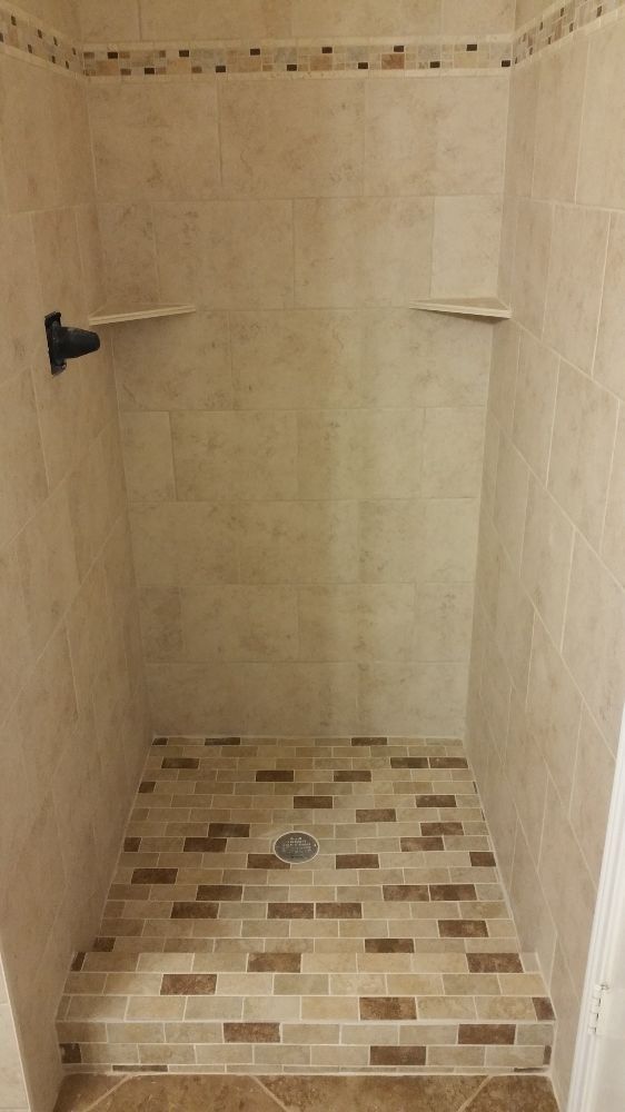 An empty shower stall with a tiled floor and a drain.