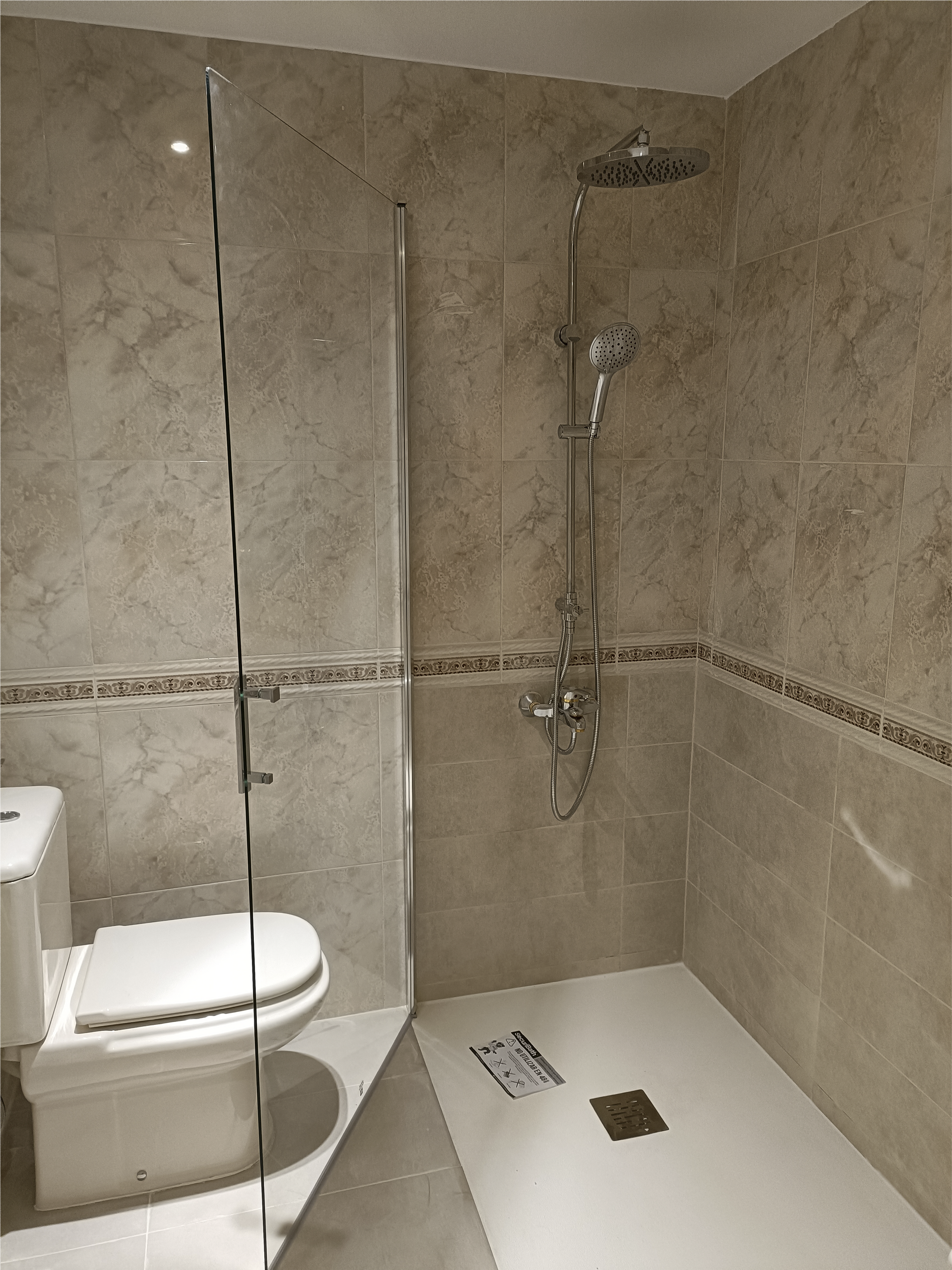 Un baño con inodoro y ducha con puerta de cristal.