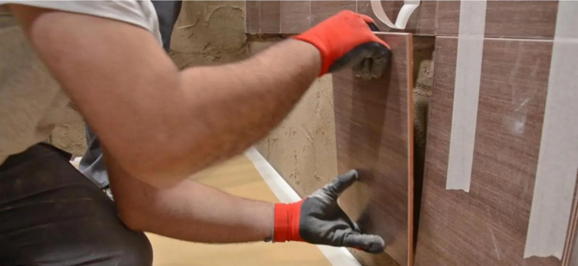 Un hombre con guantes rojos está trabajando en una pared de azulejos.