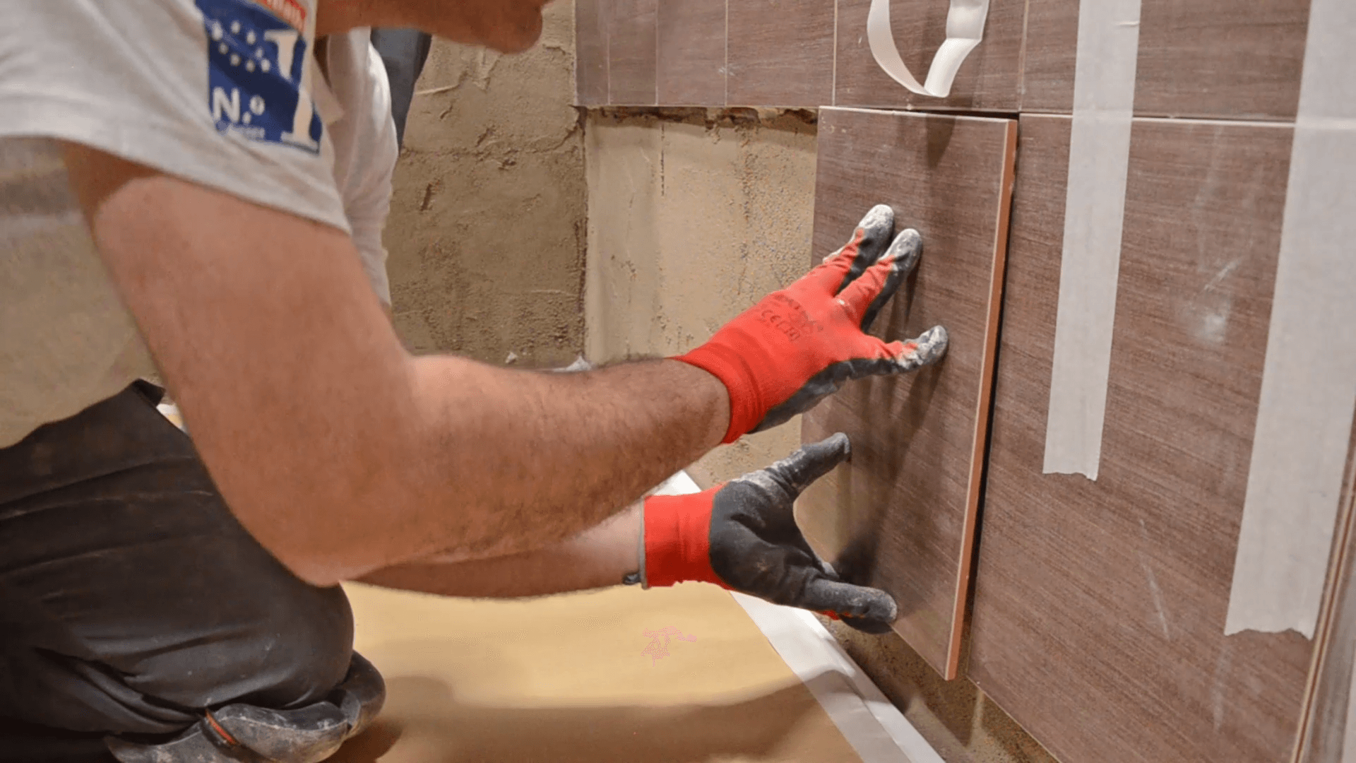 Un hombre con guantes rojos está instalando azulejos en una pared.