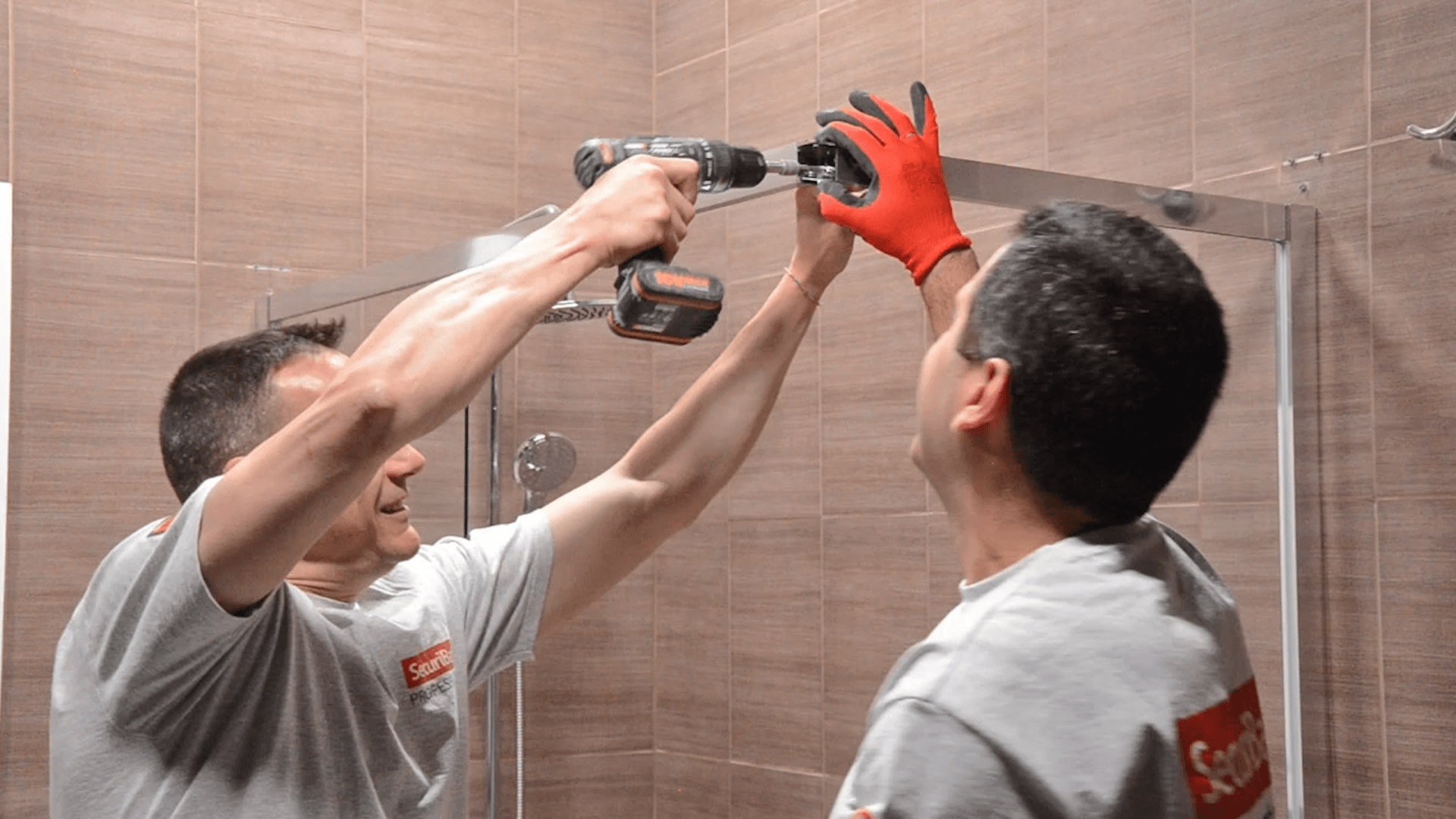 Dos hombres están instalando una puerta de ducha en un baño.