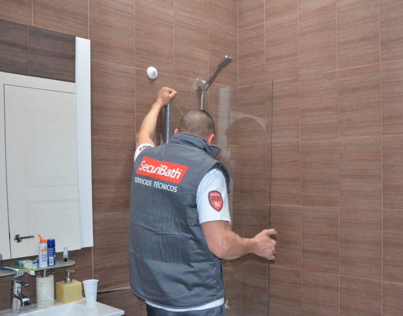 Un hombre está instalando una puerta de ducha en un baño.
