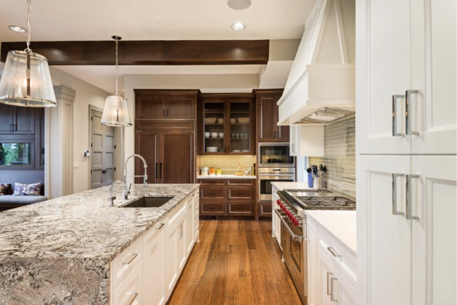 Una cocina con sobres de granito, pisos de madera, gabinetes blancos y electrodomésticos de acero inoxidable.