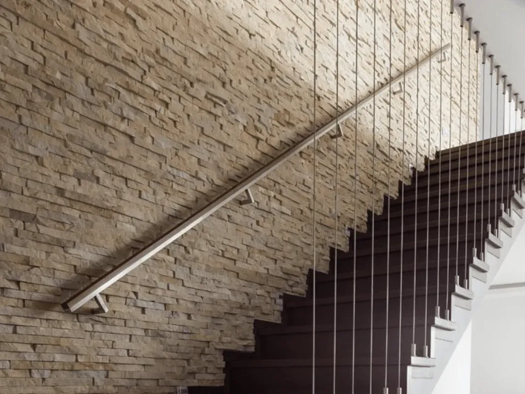 Una escalera con barandilla de acero inoxidable contra una pared de ladrillo.