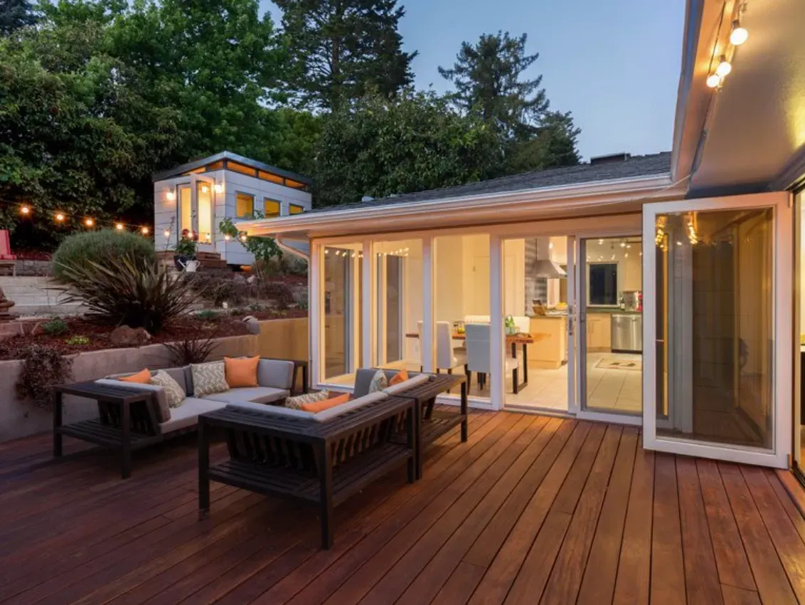 Una terraza de madera con un sofá y sillas frente a una casa.