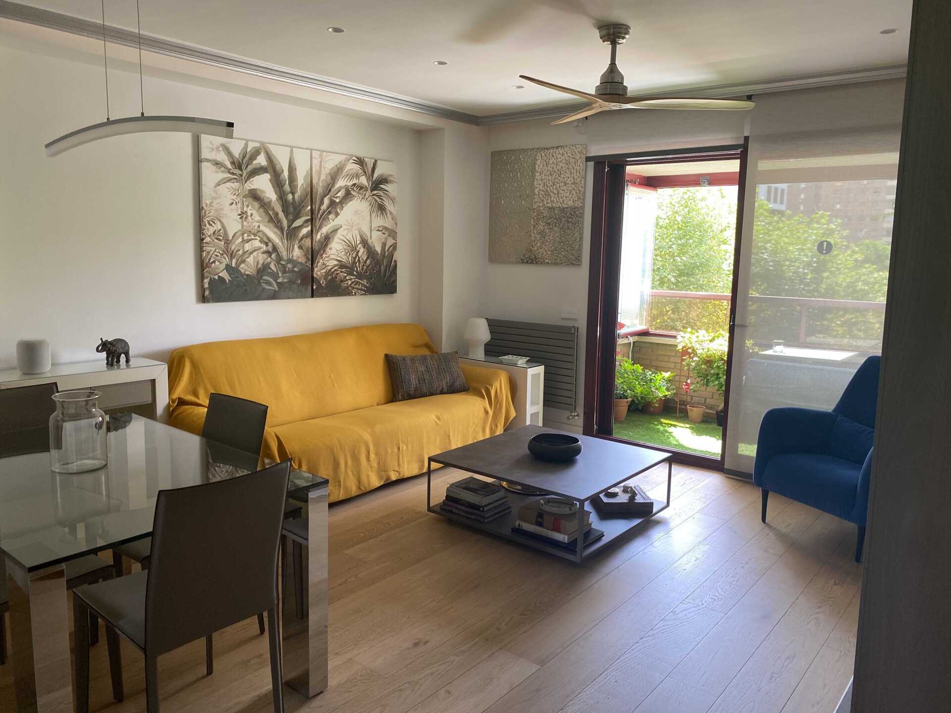Una sala de estar con un sofá amarillo, una mesa, sillas y un ventilador de techo.