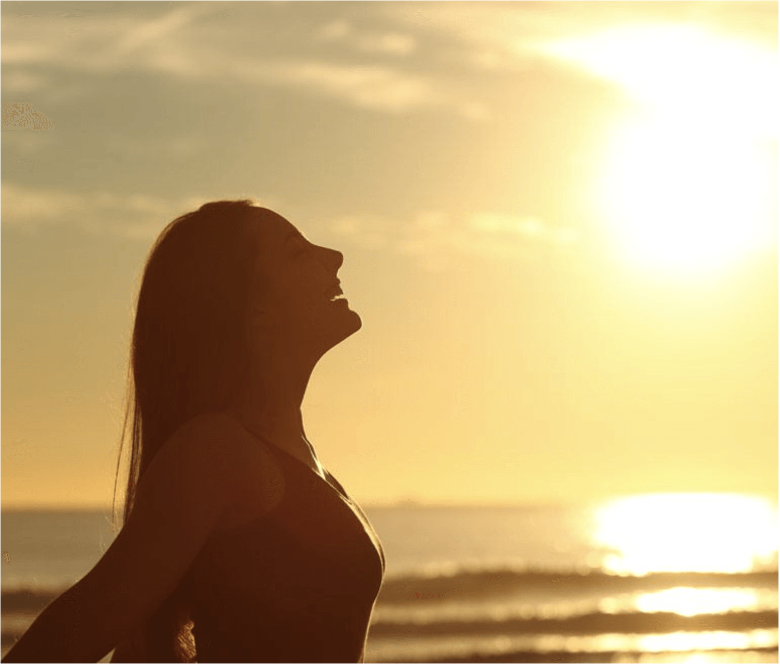 Una mujer está parada en la playa con los brazos extendidos al atardecer