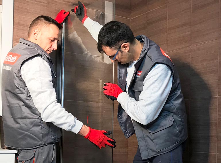 Dos hombres están trabajando en la puerta de la ducha de un baño.