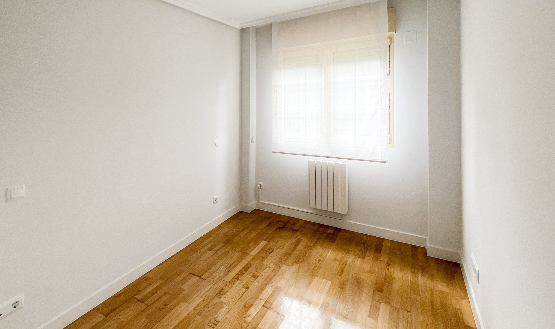 Una habitación vacía con suelos de madera y paredes blancas.