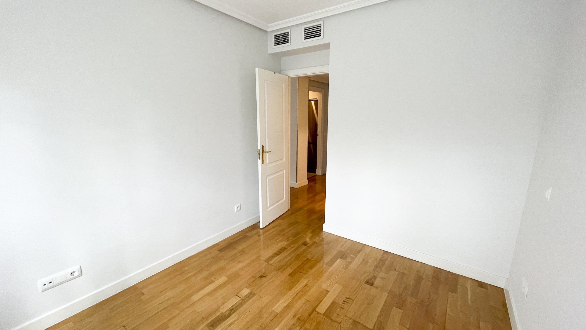 Una habitación vacía con suelos de madera y paredes blancas.
