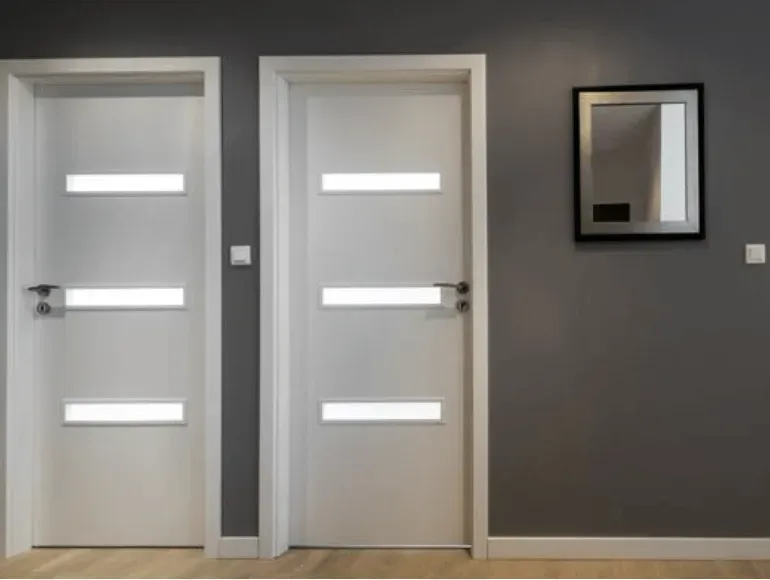 Un pasillo con dos puertas blancas y un espejo en la pared.