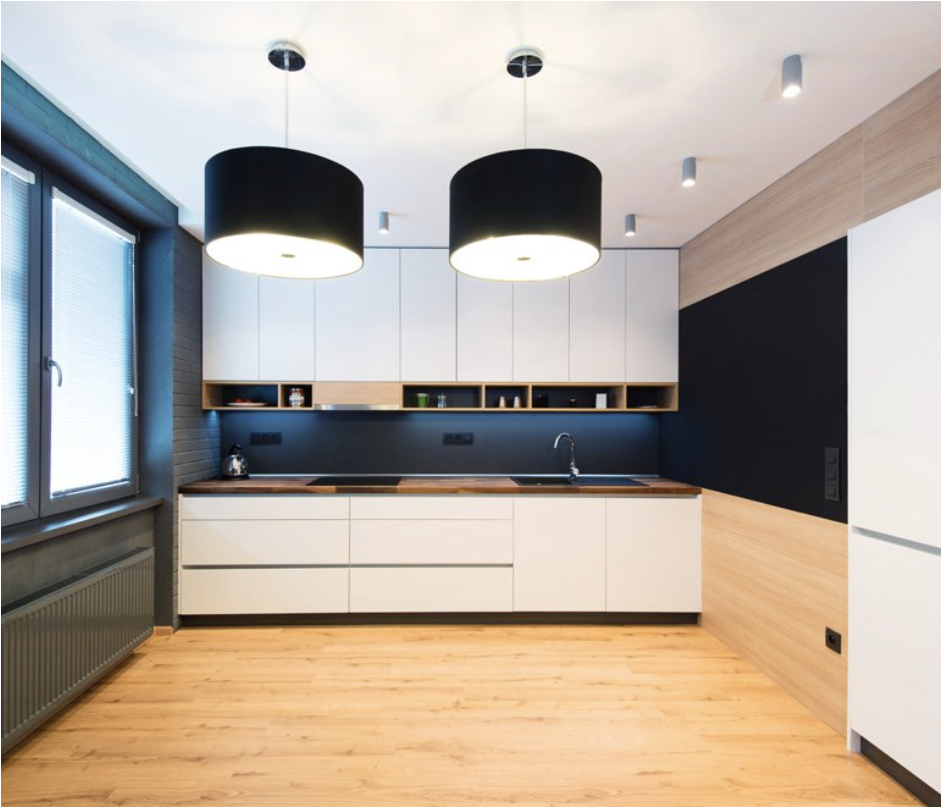 Una cocina con gabinetes blancos y luces colgantes negras.