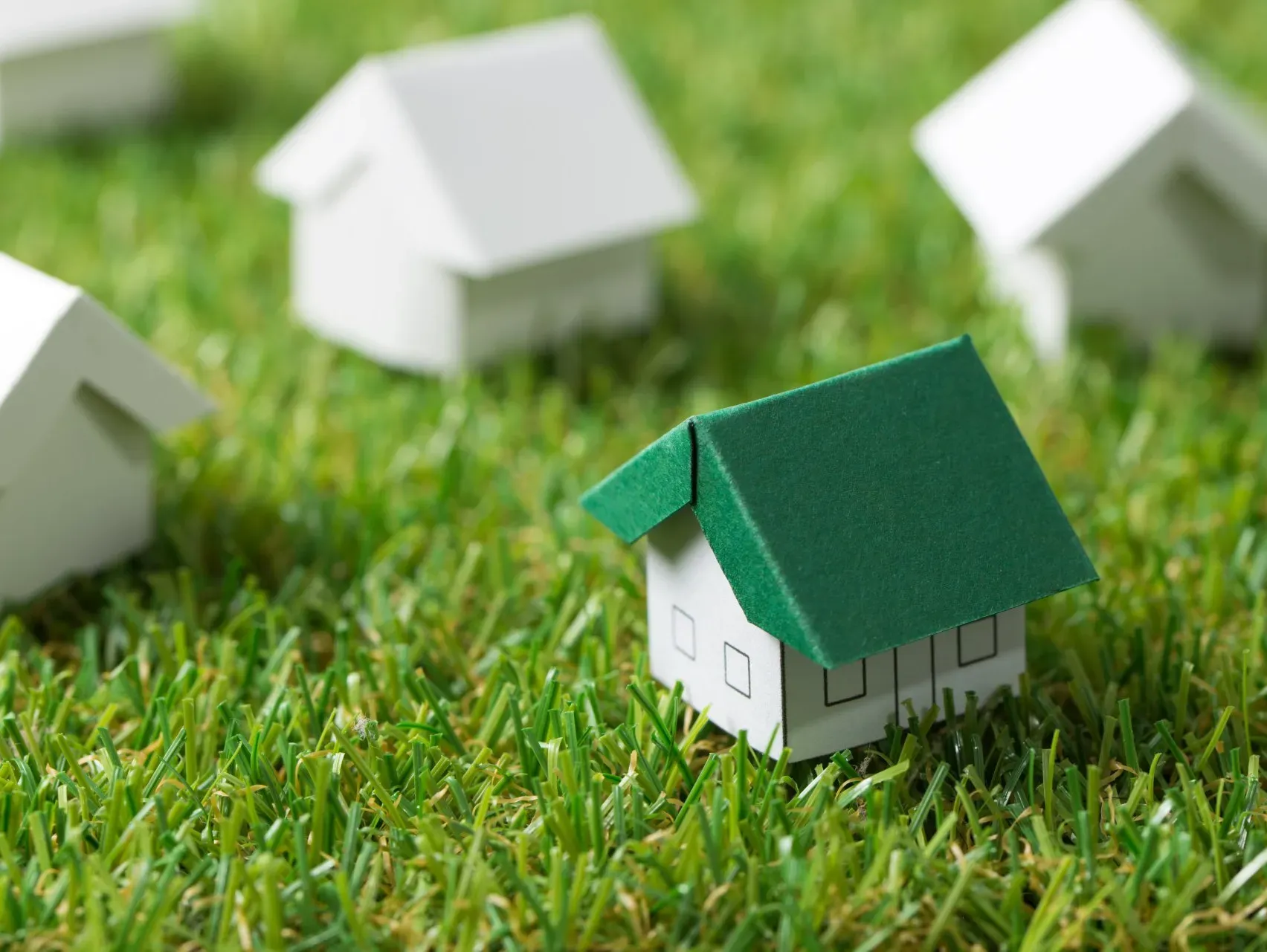 Una pequeña casa de papel con un techo verde se encuentra en lo alto de un exuberante campo verde.