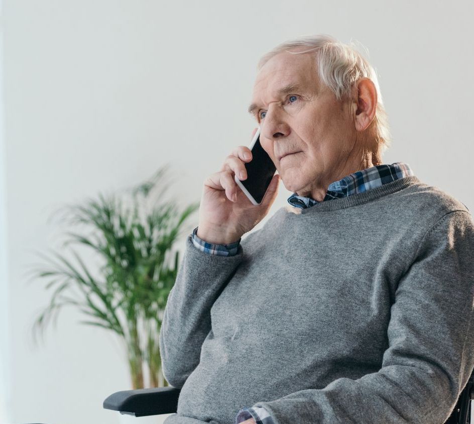 Un hombre mayor está sentado en una silla hablando por un teléfono móvil.
