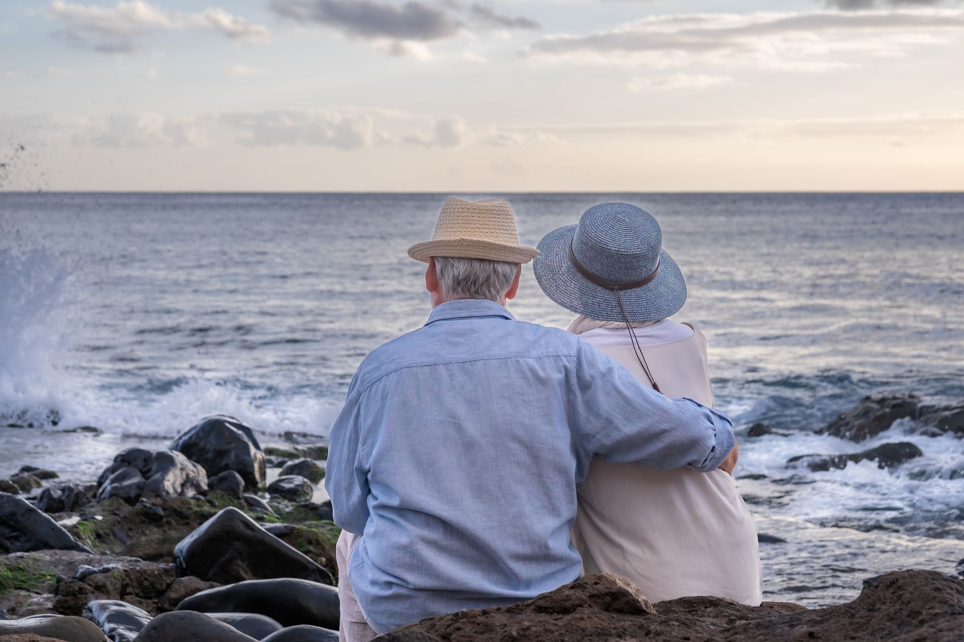 Una pareja de ancianos está sentada en la playa mirando el océano.