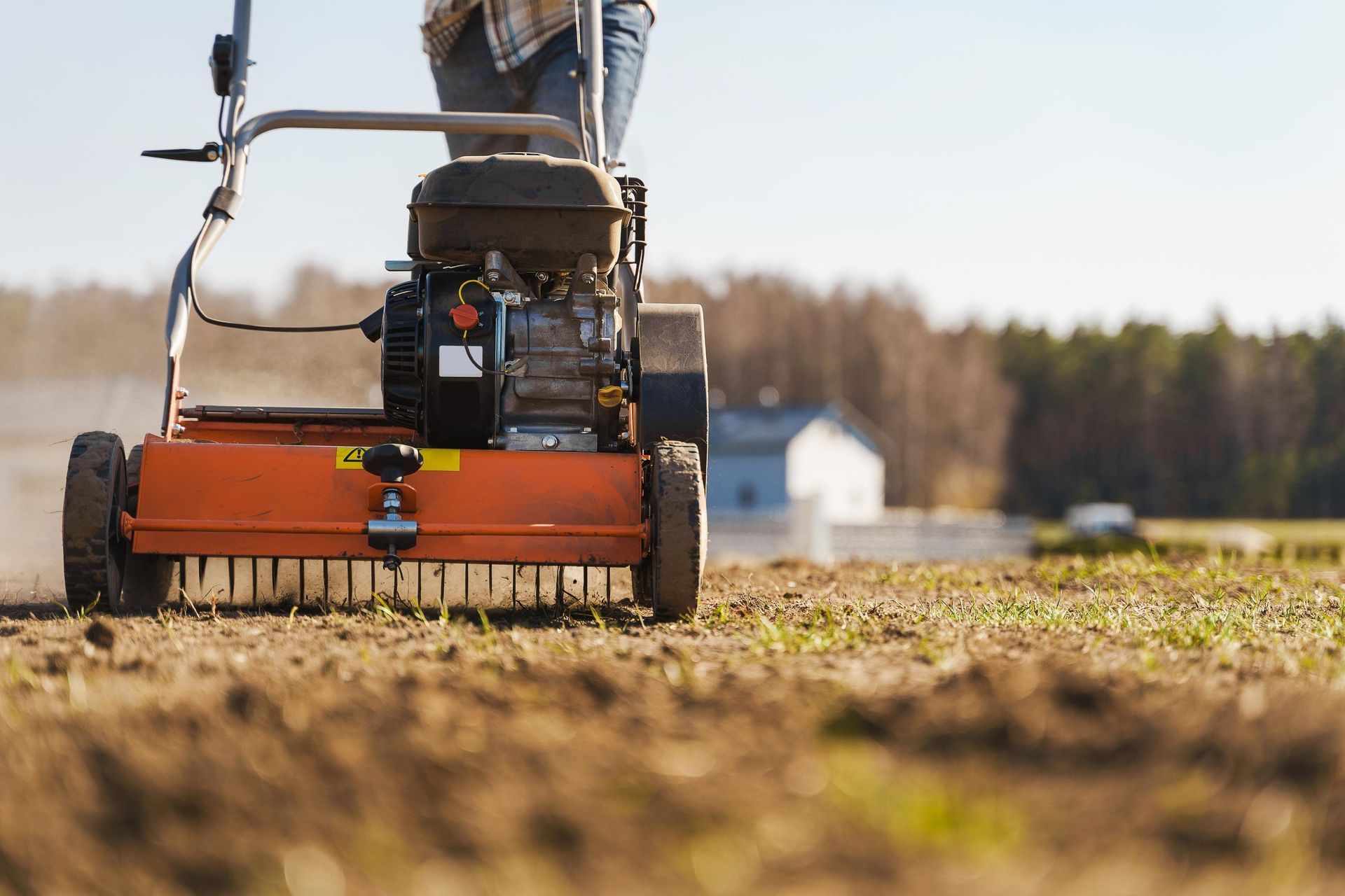 Person using a powered lawn aerator on a field, kicking up soil.