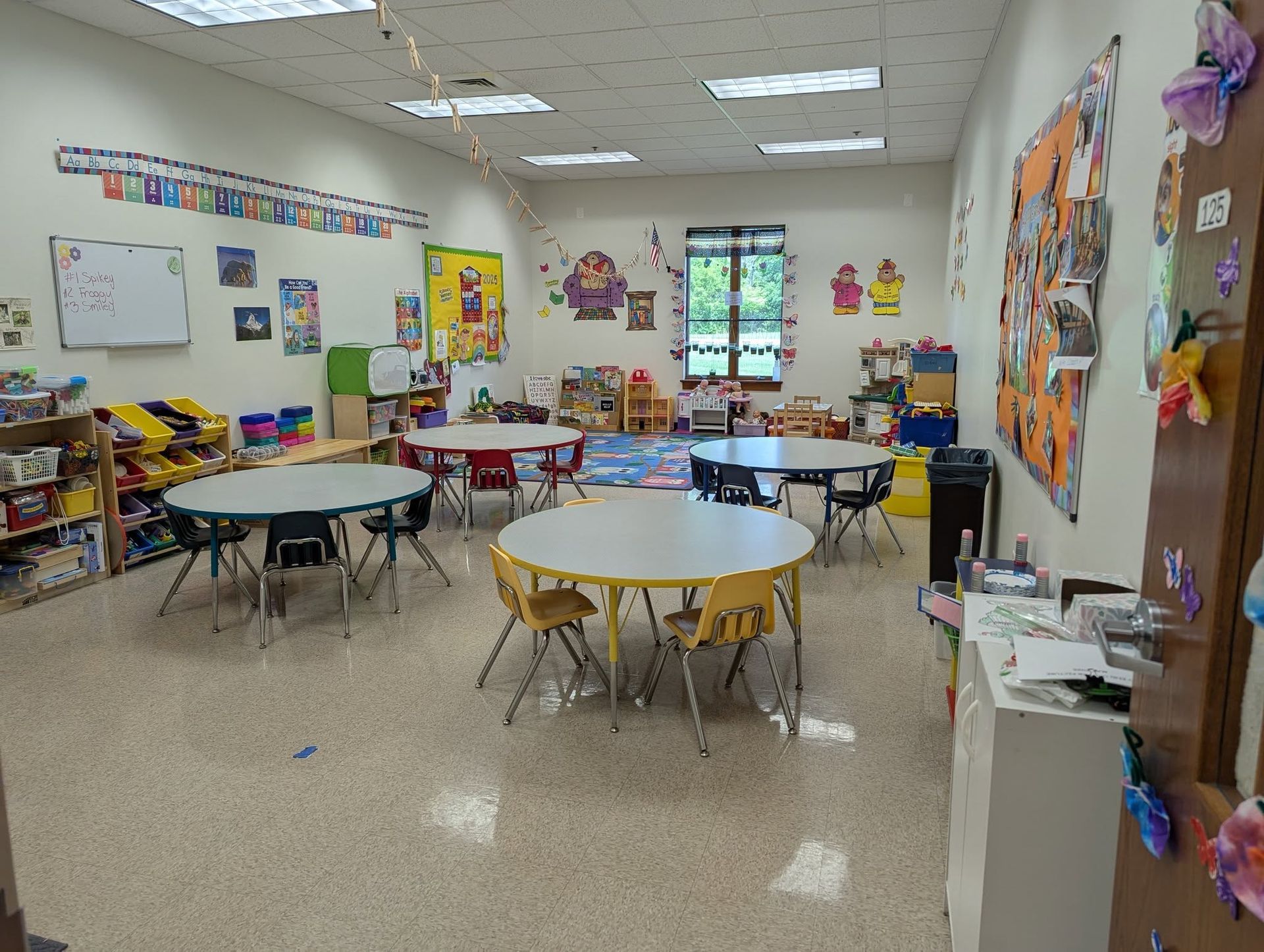 A classroom with tables and chairs and a whiteboard on the wall.