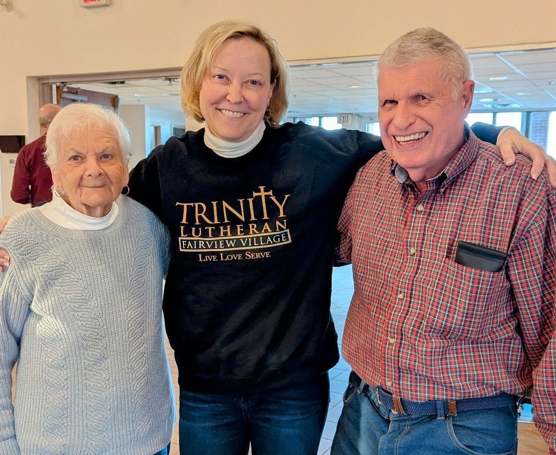 A woman wearing a Trinity Lutheran Fairview Village shirt is posing for a picture with two men.