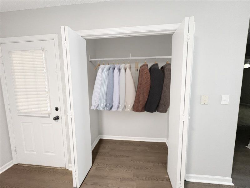 Open closet with hanging clothes beside a white door in a bright room.