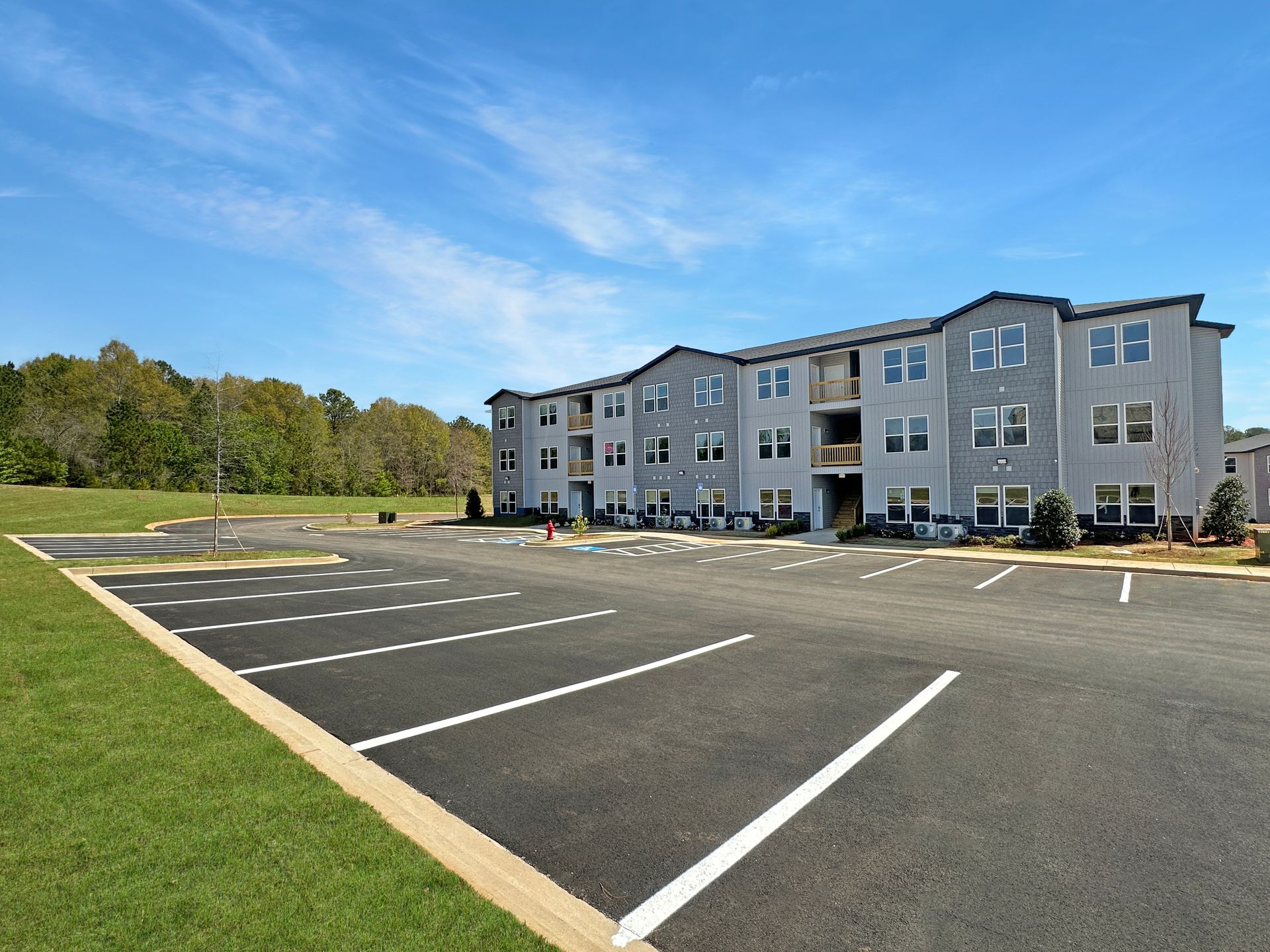 Empty parking lot beside a gray apartment building under a blue sky.