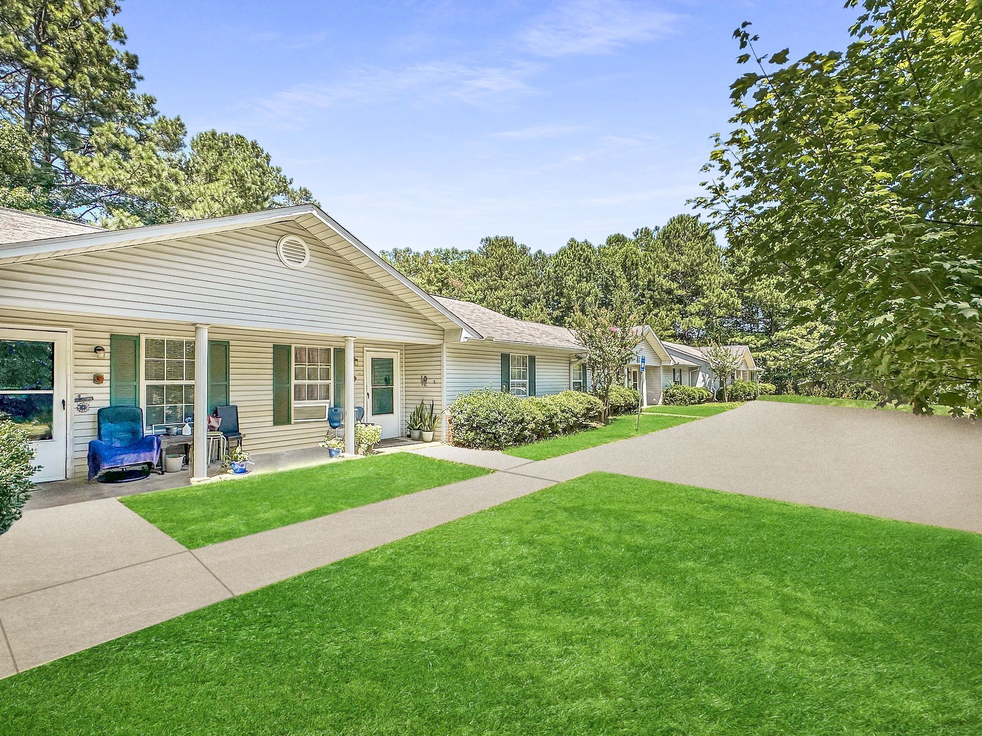 Single-story suburban house with a front porch, green lawn, and driveway under a blue sky
