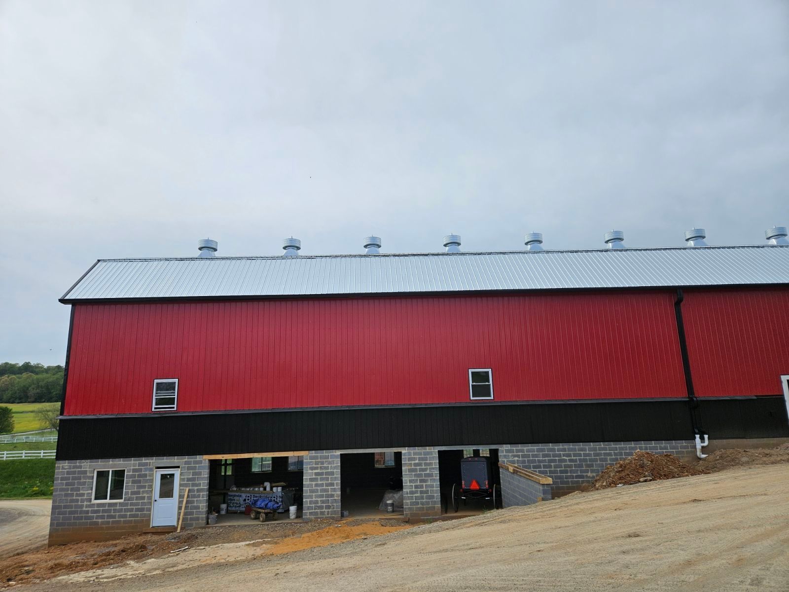 A large red barn with a black roof is sitting on top of a dirt hill.