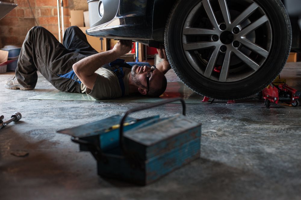 A Man In Blue Overalls Is Holding A Wrench Under Car — Jasco Automotive In Bowen, QLD