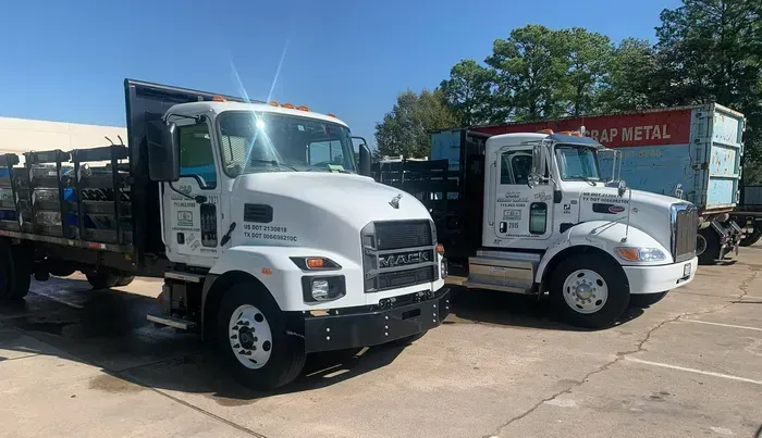 Two white flatbed trucks parked side by side in a sunny lot