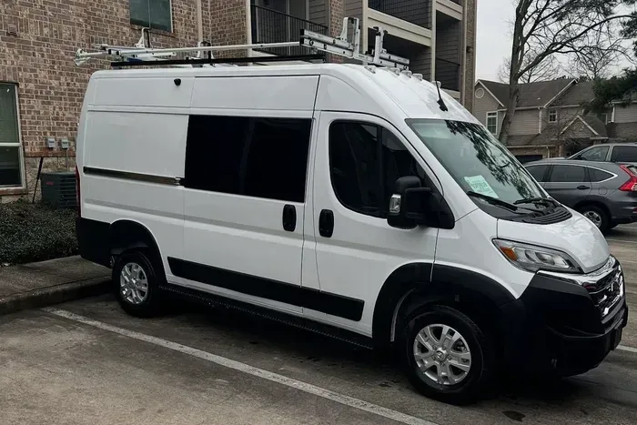 White cargo van parked on a wet street beside brick apartment buildings