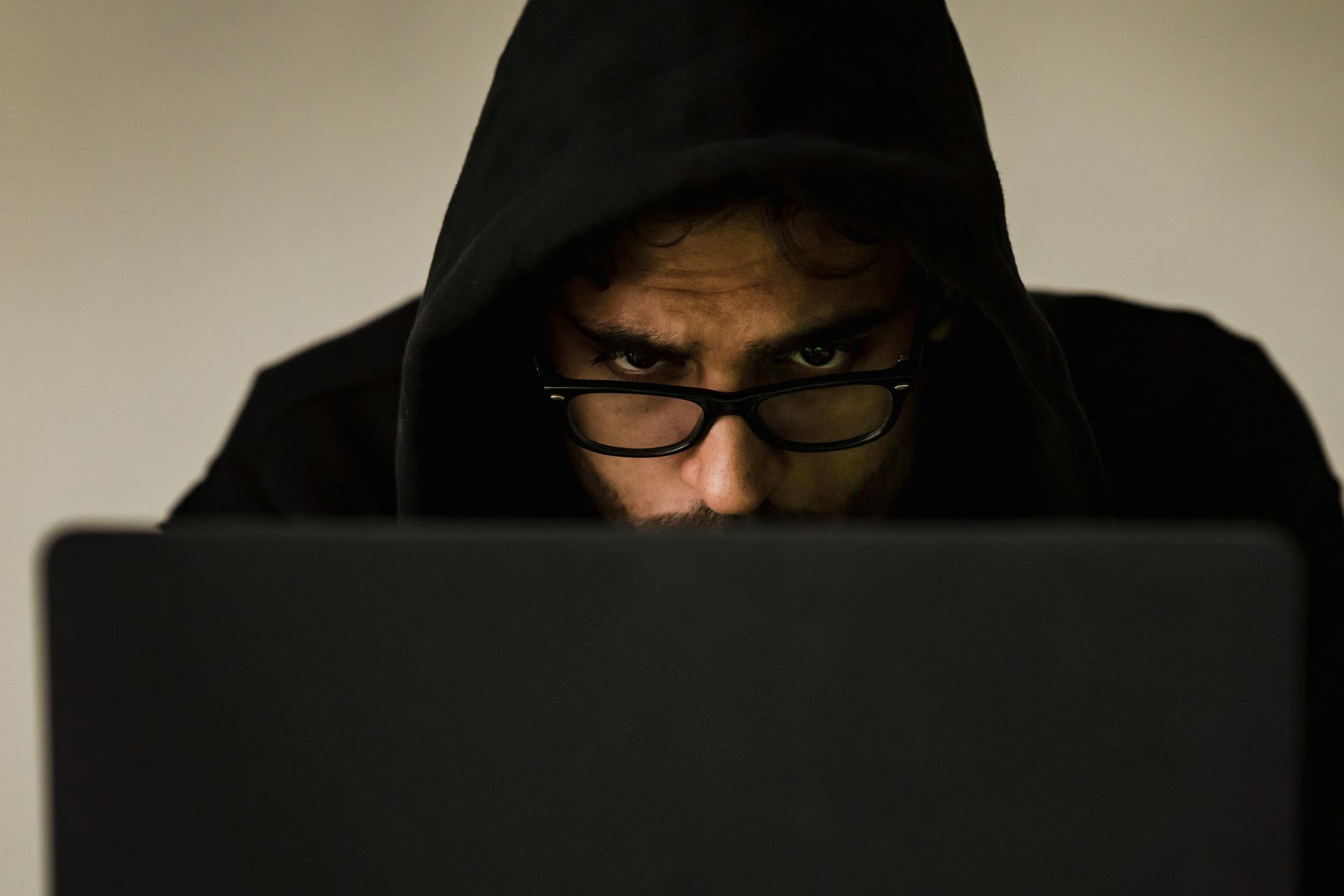 A man in a hoodie and glasses is looking at a laptop computer.