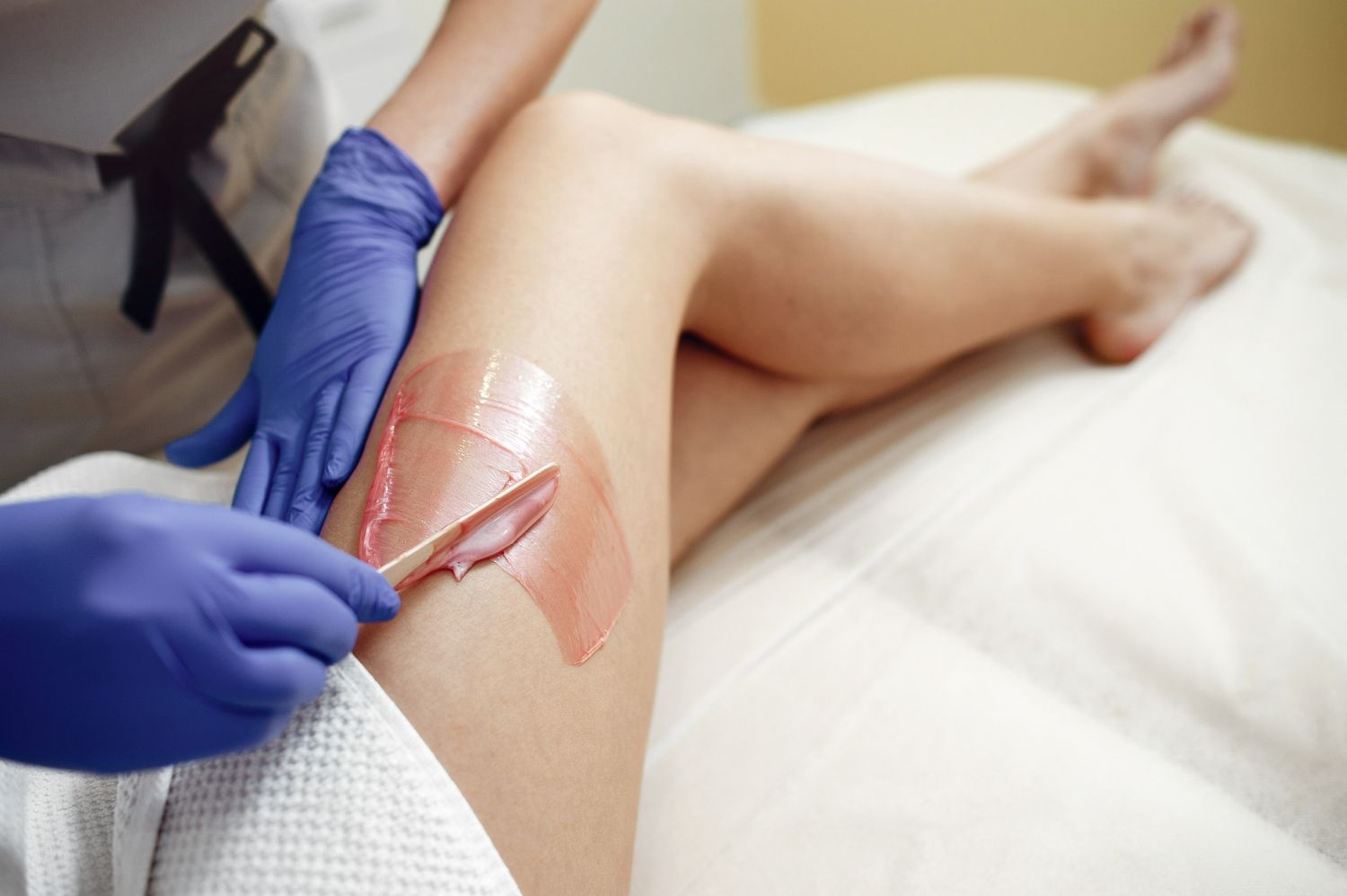 A person waxing a leg with pink wax in a spa setting.
