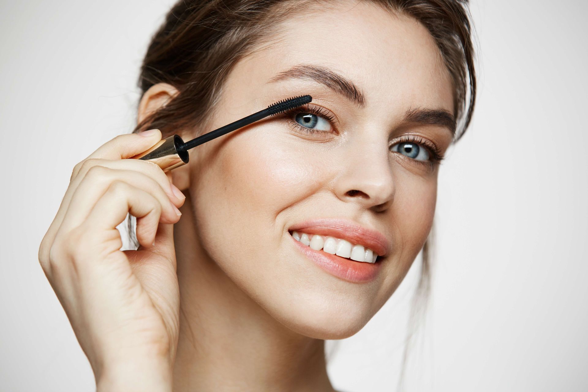 a woman is smiling while applying mascara to her eye .