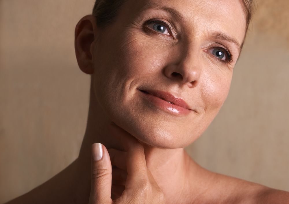 A woman is touching her neck with her hand and smiling.