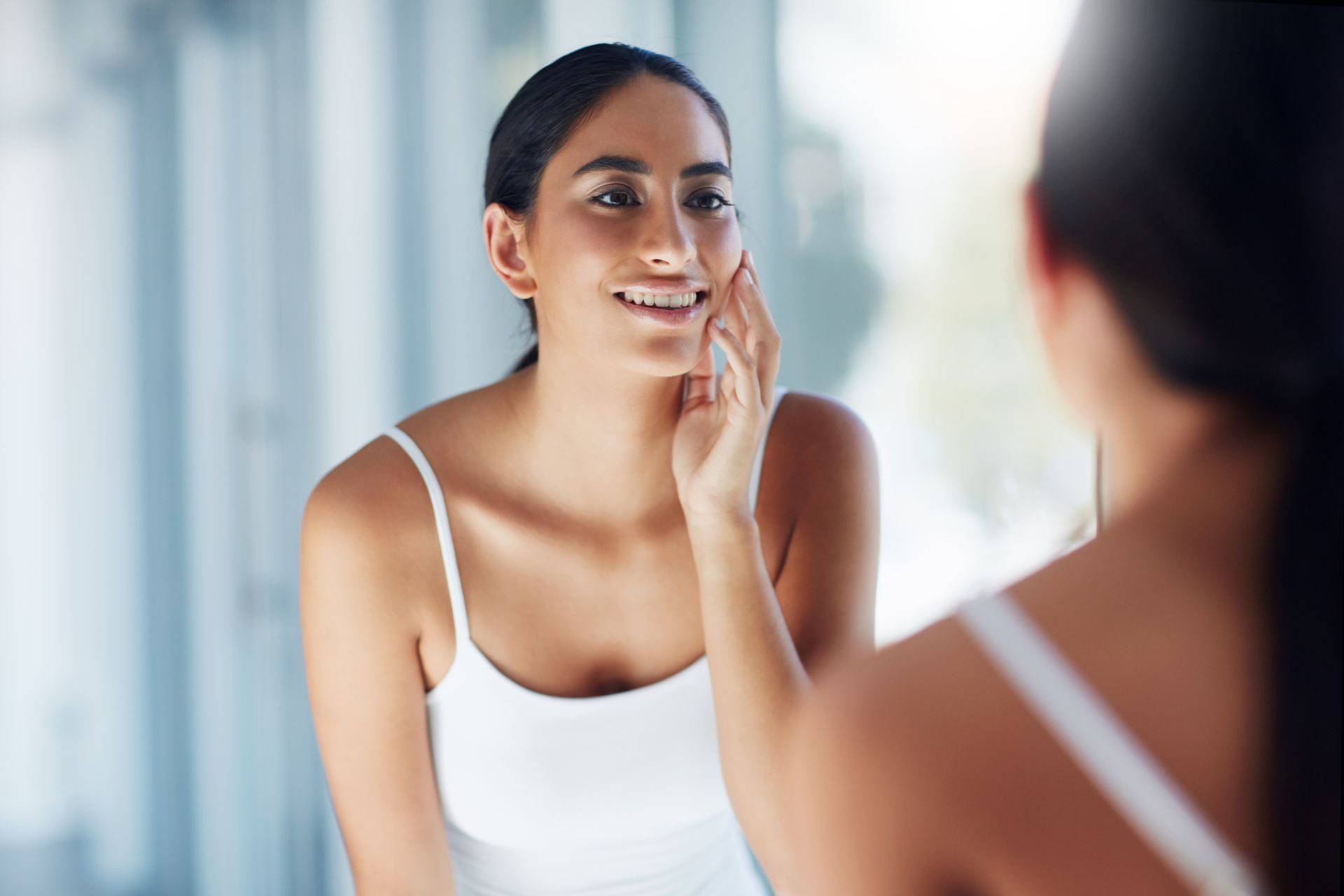 A woman is looking at her face in the mirror.