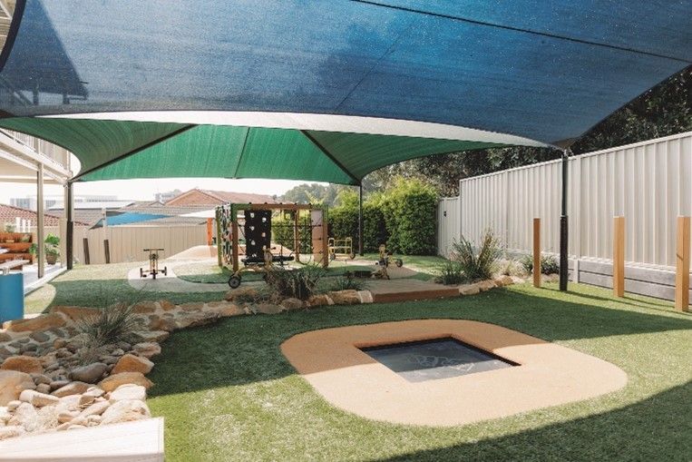 A playground with a trampoline under an umbrella.