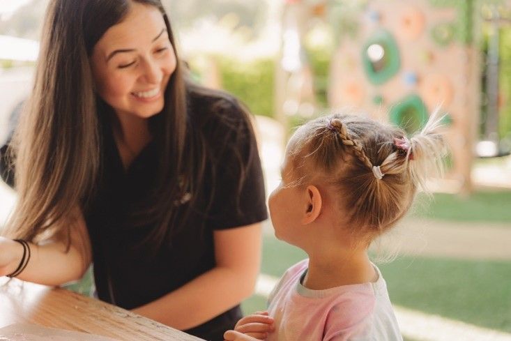 A woman is talking to a little girl who is sitting at a table.