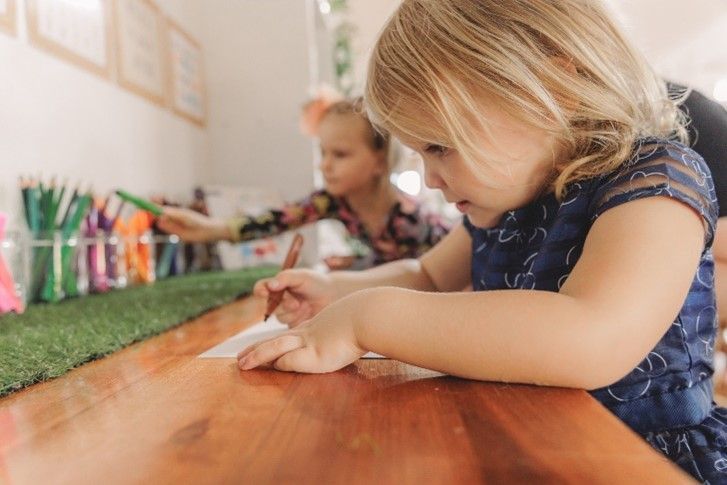 A little girl is sitting at a table drawing with a pencil.