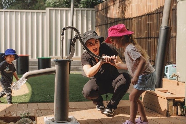 A woman and two children are playing with a water pump.