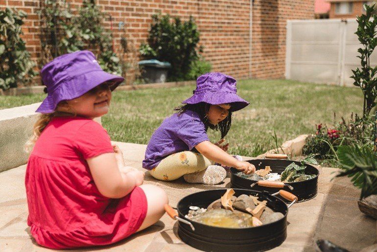 Two little girls are playing in the dirt in a backyard.